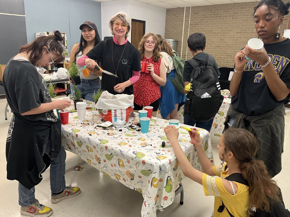 students gather at table to plant small plants in individual cups